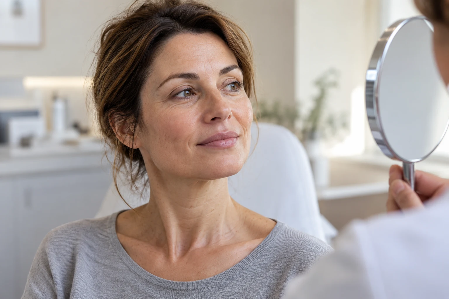 Biorivitalizzazione del viso: cosa sapere prima Donna osserva il proprio viso in uno specchio durante una consulenza sulla pelle