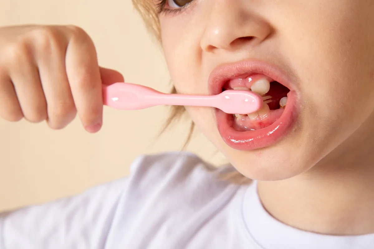 Primo piano di un bambino che spazzola i denti con uno spazzolino rosa, foto illustrativa della guida dello Studio Dentistico Baldari sulla prevenzione della carie.